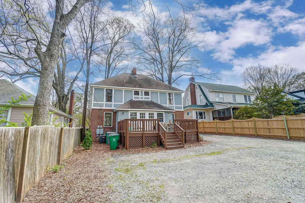 An inviting exterior view of a two-story house with a spacious wooden deck framed by leafy trees. The gravel driveway adds to the homey feel, and the outdoor space is clearly set up for gatherings and relaxation, echoing the sense of home base described in the text.