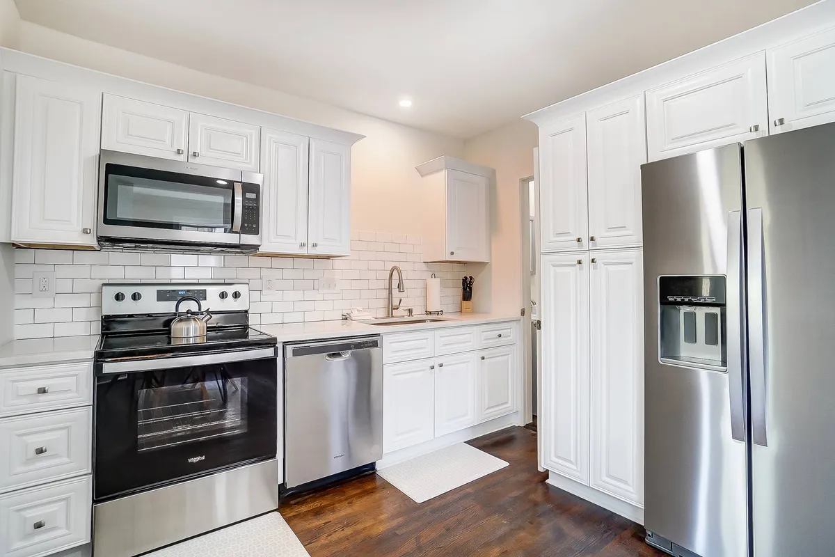 A bright and welcoming kitchen featuring a stainless steel refrigerator, modern black stove, white cabinetry, and a sleek subway tile backsplash. The spacious countertops offer ample space for meal preparation. Natural light streams in, enhancing the freshness and functionality of the kitchen.