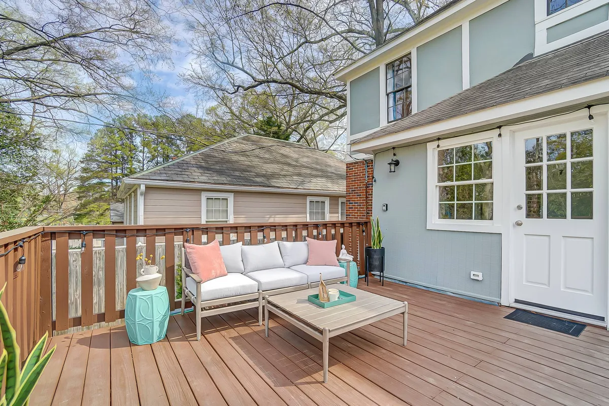 A tranquil outdoor lounge with a sofa, coffee table, and decorative vase set against a backdrop of trees and dappled sunlight. The setup encourages intimate gatherings, socializing, or enjoying the peaceful ambiance—just as described for evenings around the fire pit or casual relaxation.
