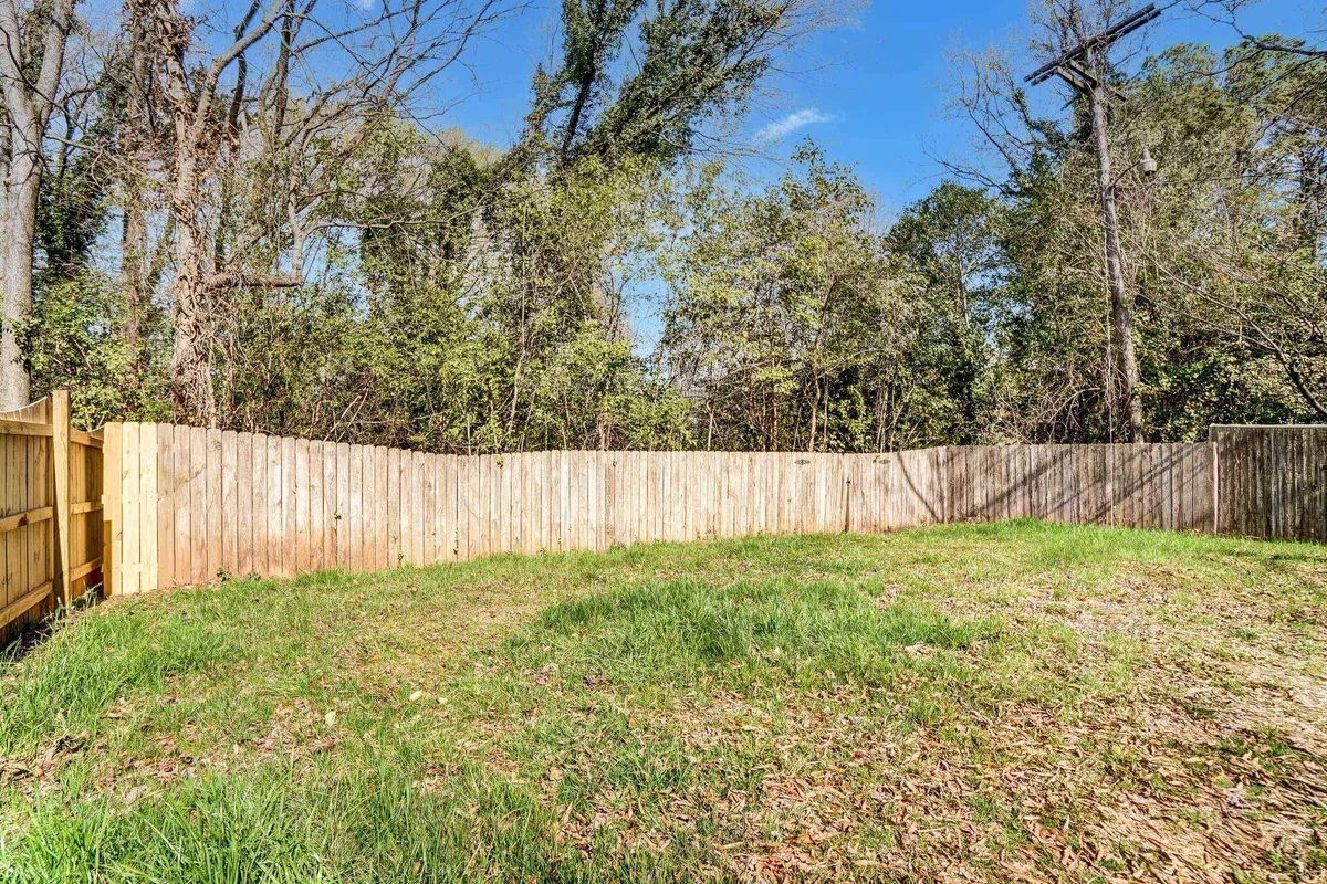 A lush, fenced yard with thick grass and mature trees surrounds the space, offering a safe and relaxed environment. The openness is ideal for children or pets to play, gardening, and gathering outdoors.