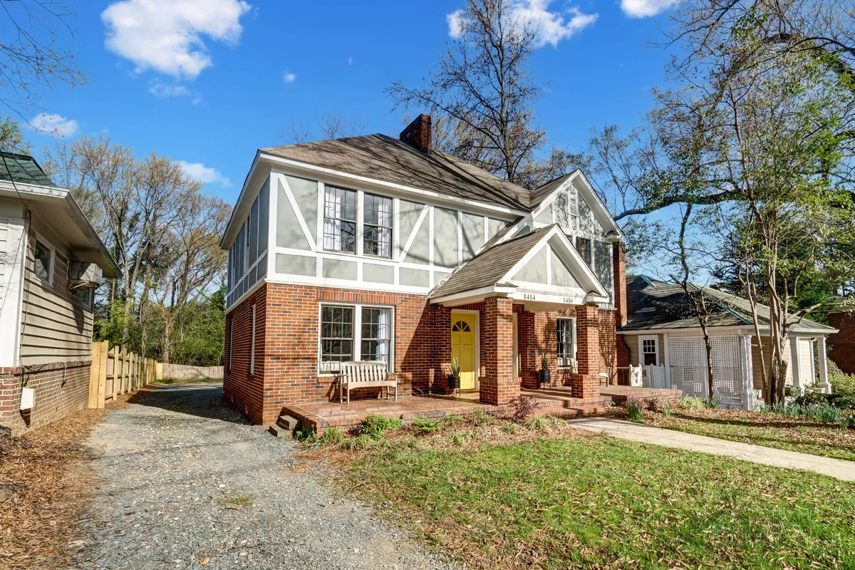 This image displays the inviting front porch with a cheerful yellow door, brick facade, and cozy steps, surrounded by greenery. The scene is bathed in natural light suggesting a tranquil, welcoming atmosphere in a historic neighborhood.