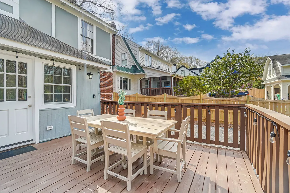 An inviting exterior dining area with a table and potted plants, surrounded by a fence and neighboring houses. The setting is cheerful and ideal for outdoor meals, gatherings, or simply relaxing.