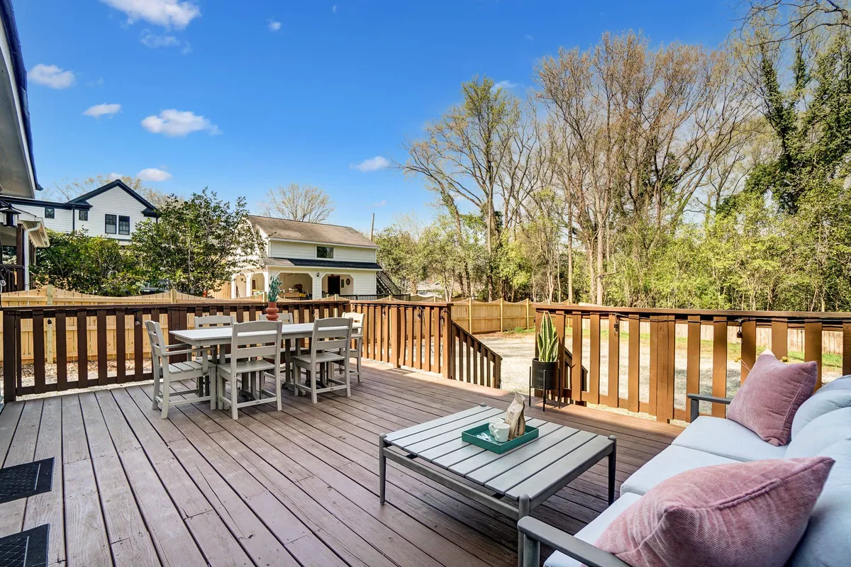 This image showcases a spacious backyard with a dining table, outdoor couch, lush greenery, and a fenced yard. The area feels welcoming and open, providing plenty of room for gatherings and activities. The fenced aspect suggests safety and space for pets, while the greenery and comfortable furniture create an inviting atmosphere for socializing or relaxing.